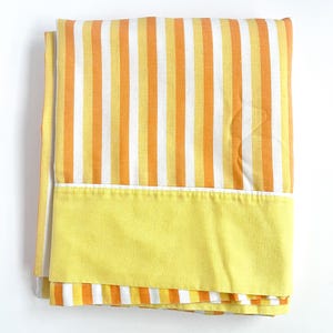 May include: A yellow and orange striped bed sheet with a solid yellow border. The sheet is folded and appears to be made of cotton.