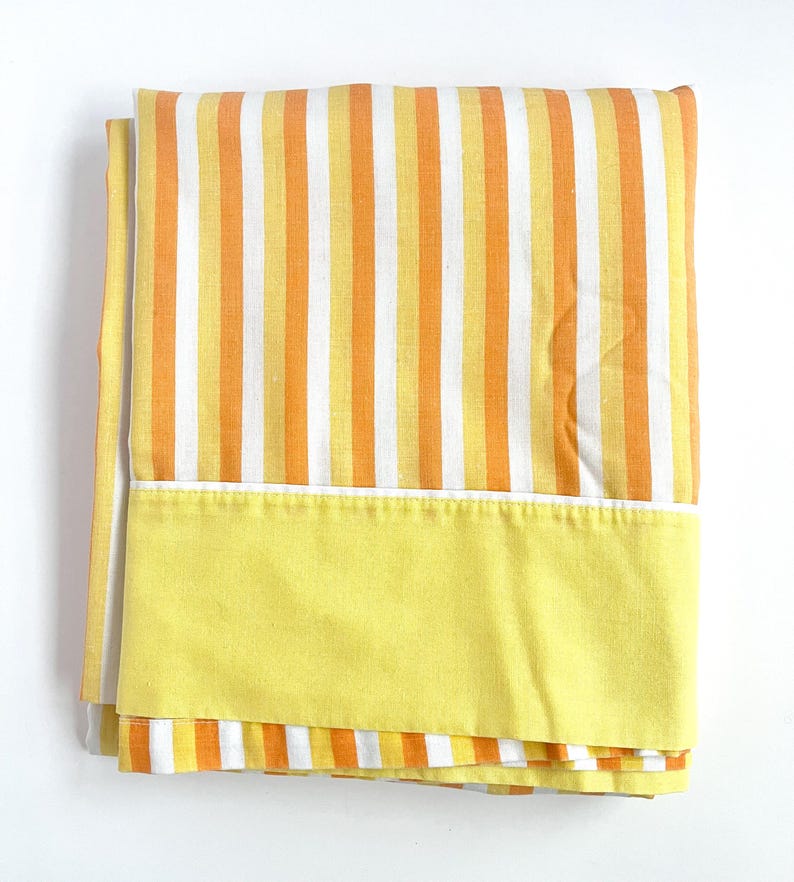 May include: A yellow and orange striped bed sheet with a solid yellow border. The sheet is folded and appears to be made of cotton.