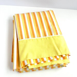 May include: A folded yellow and orange striped bed sheet with a solid yellow border.