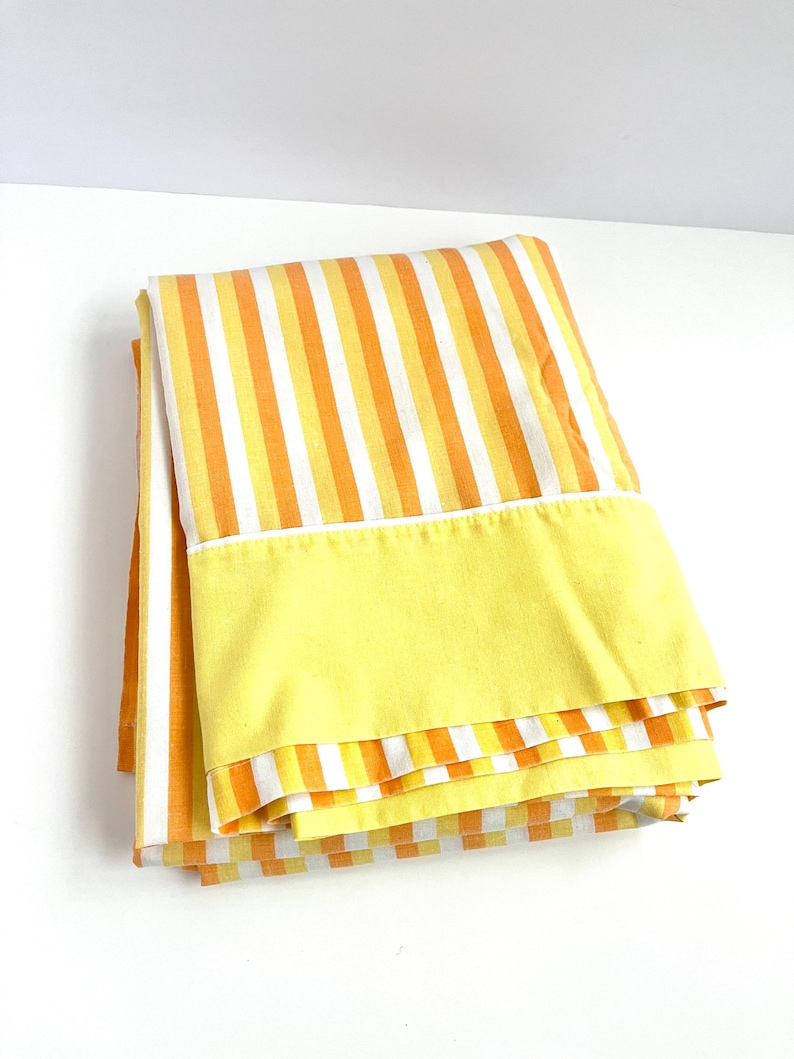 May include: A folded yellow and orange striped bed sheet with a solid yellow border.