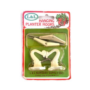 May include: Vintage package of L&L Hanging Planter Hooks. The package features two sets of hooks, each with a decorative, off-white, heart-shaped design. The package has a green and red border with the text "L&L Hanging Planter Hooks".