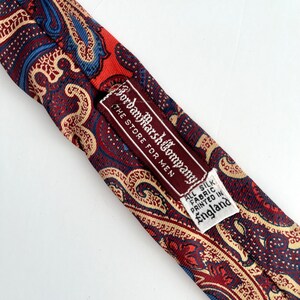 May include: A red, blue, and cream paisley patterned silk tie with a brown label that reads "Jordan Marsh Company, The Store for Men, All Silk Fabric Printed in England."