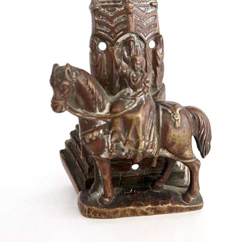 May include: A bronze sculpture of a person riding a horse. The person is wearing a long robe and is holding a staff. The horse is standing on a base with a decorative design. The sculpture is in a vintage style.