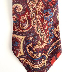 May include: A red, blue, and beige paisley patterned tie. The tie has a pointed tip and a classic design.
