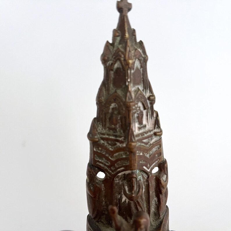 May include: A detailed bronze sculpture of a church with a pointed spire and intricate carvings. The sculpture is a miniature replica of a real church.