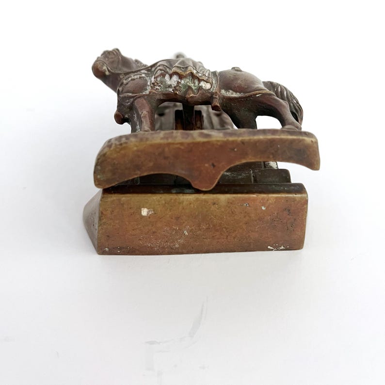 May include: A bronze sculpture of a rider on horseback, the horse is standing on a base with a decorative design. The sculpture is a paperweight.