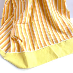 May include: Yellow and orange striped fabric with a solid yellow border. The fabric is folded and has a soft, textured appearance.
