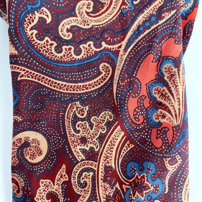 May include: A red, blue, and beige paisley patterned fabric with a repeating design.