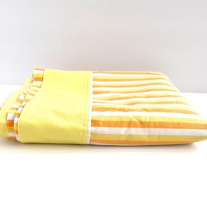 May include: A folded yellow and orange striped bed sheet with a solid yellow border.