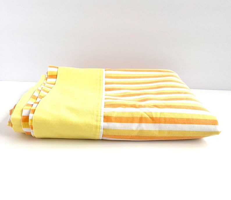 May include: A folded yellow and orange striped bed sheet with a solid yellow border.