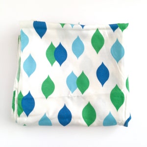 May include: White fabric with a repeating pattern of teardrop shapes in shades of blue and green.