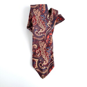May include: A paisley patterned tie in shades of brown, red, blue, and cream.