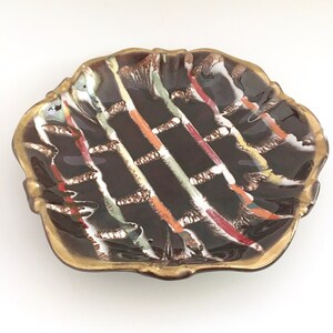 May include: A brown ceramic dish with a scalloped edge and a gold rim. The dish has a geometric pattern of white, red, orange, and green lines.