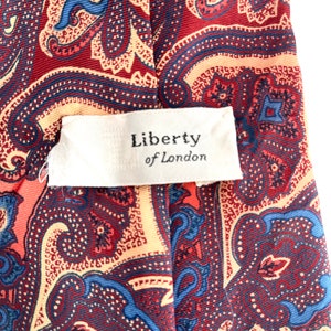 May include: A red, blue, and cream paisley patterned tie with a white tag that reads "Liberty of London".