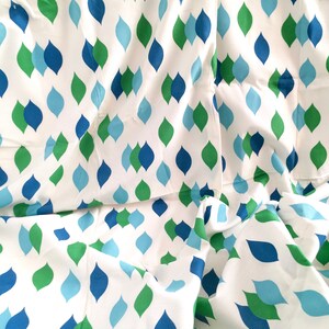 May include: White fabric with a repeating pattern of teardrop shapes in shades of blue and green.