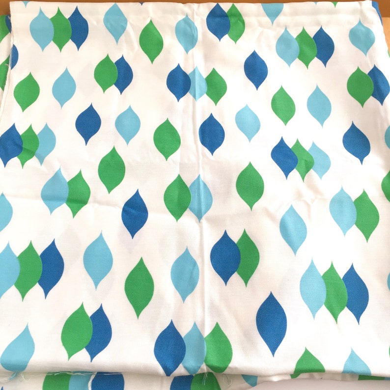 May include: White fabric with a repeating pattern of teardrop shapes in shades of blue and green.