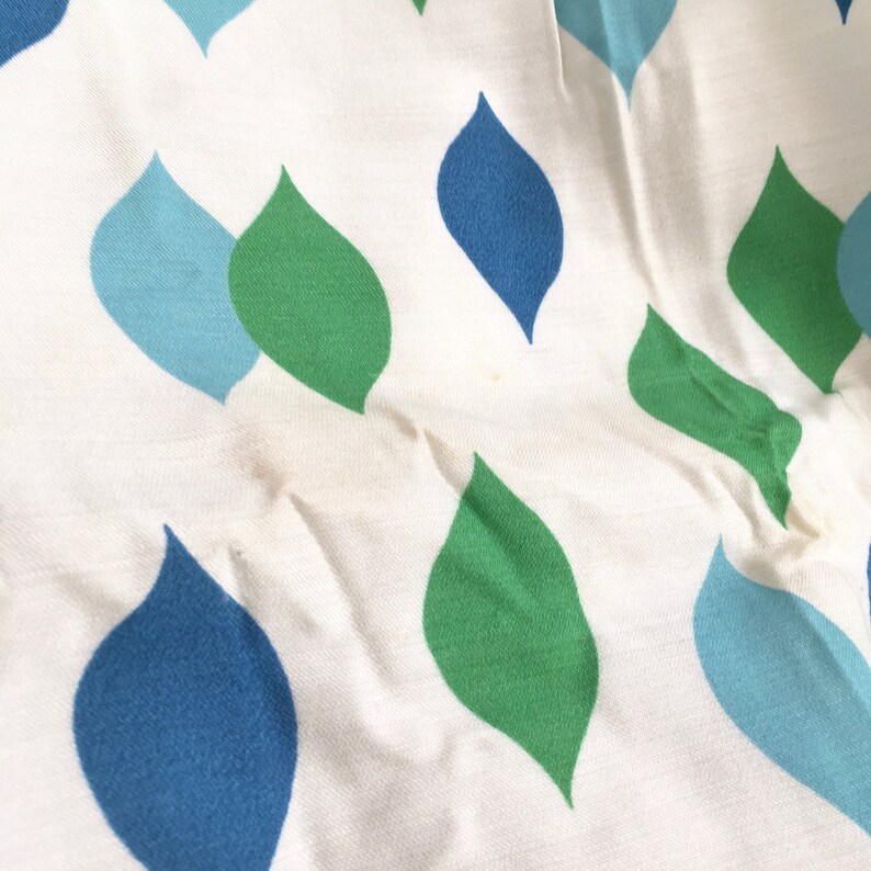 May include: White fabric with a repeating pattern of blue and green teardrop shapes.