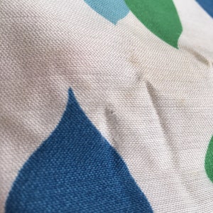 May include: Close-up of a white fabric with a blue and green geometric pattern. The fabric has a textured surface and appears to be made of cotton.