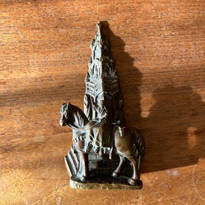 May include: A bronze door knocker in the shape of a knight on horseback riding towards a tall, ornate church.