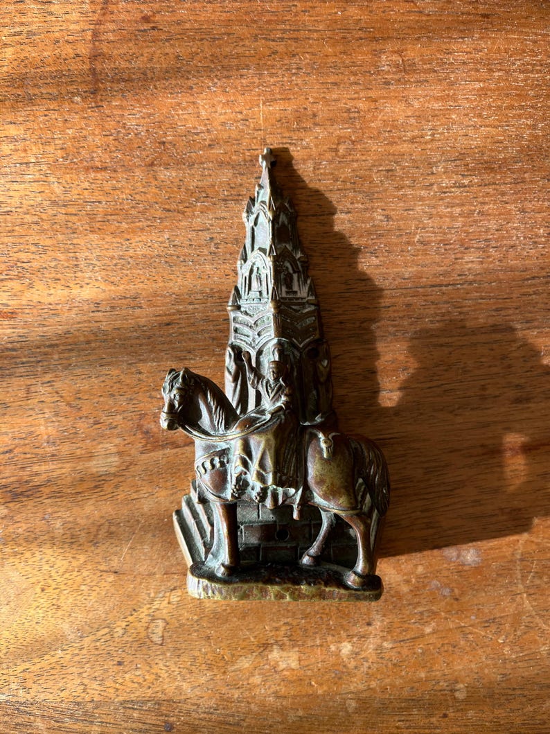 May include: A bronze door knocker in the shape of a knight on horseback riding towards a tall, ornate church.