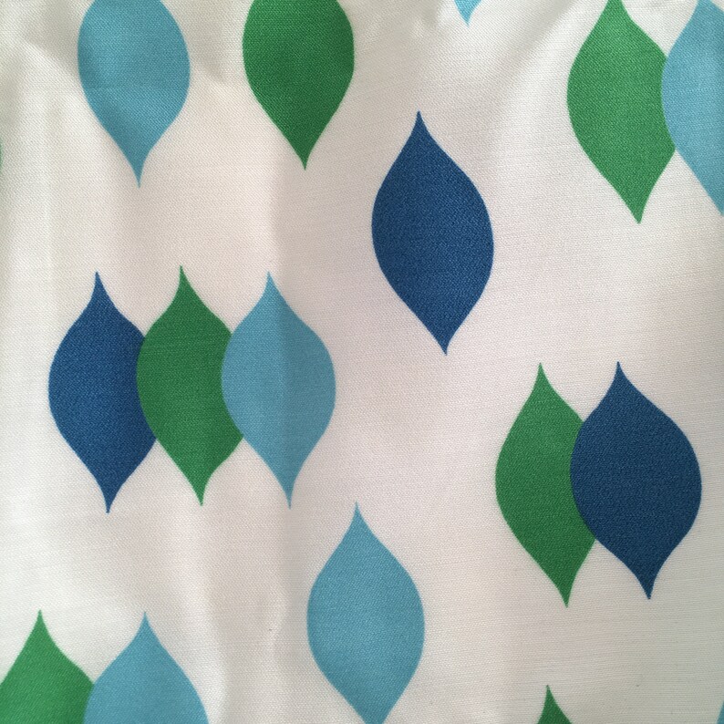 May include: White fabric with a repeating pattern of blue and green teardrop shapes.