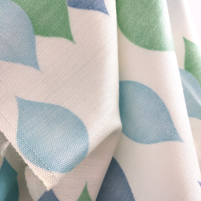 May include: White fabric with a repeating pattern of blue and green teardrop shapes.