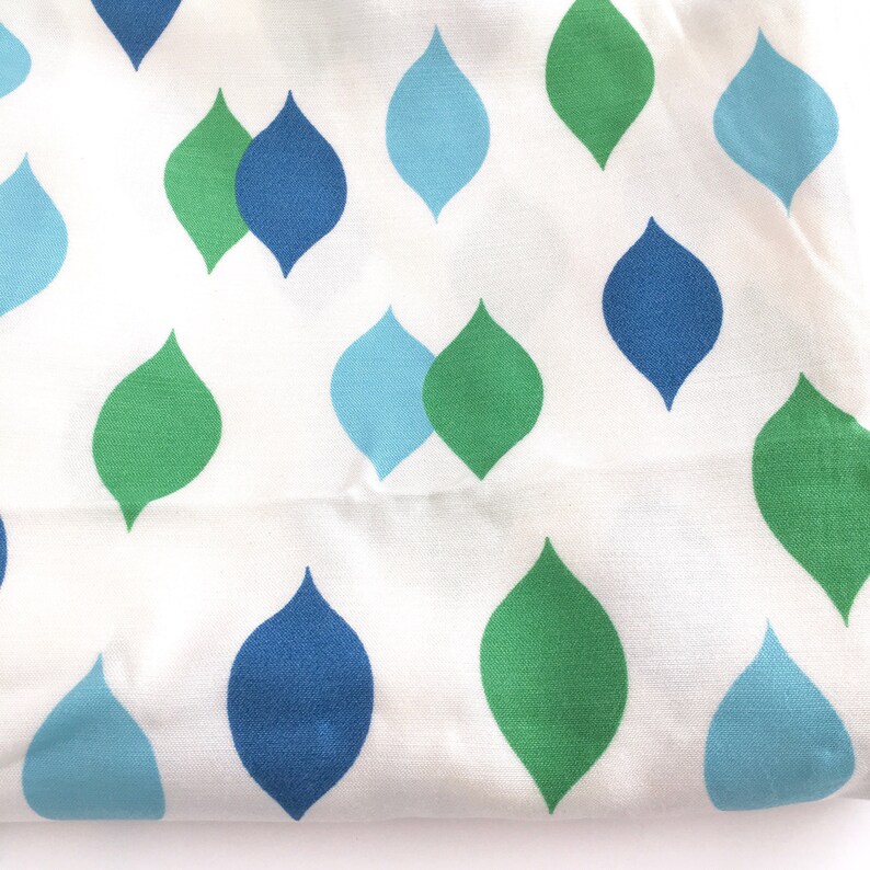 May include: White fabric with a repeating pattern of teardrop shapes in shades of blue and green.