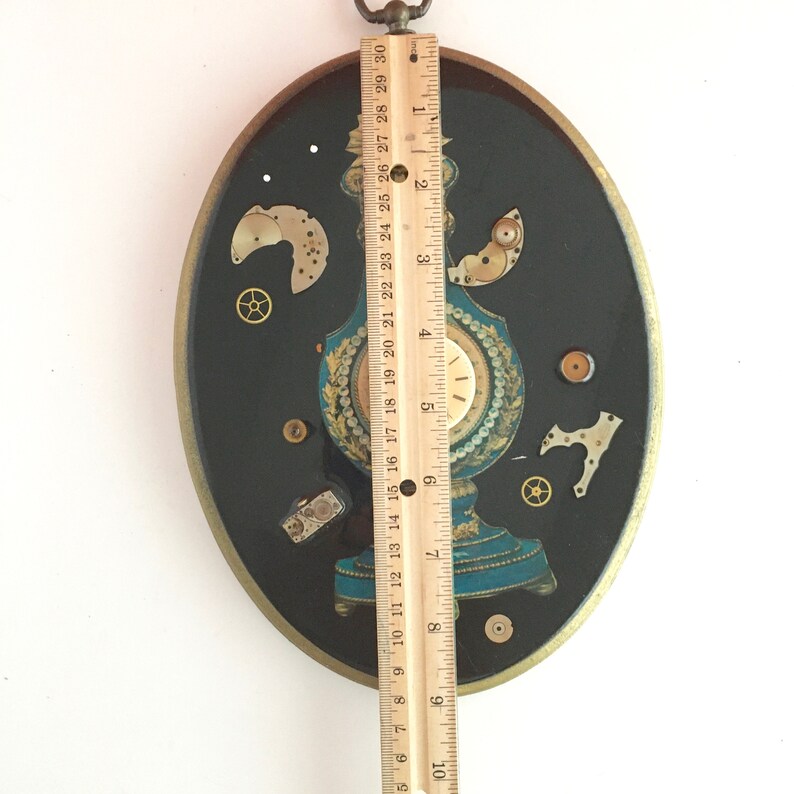 May include: A circular, black and gold framed wall art piece with a clock face and various watch parts embedded in resin. The clock face is white with black Roman numerals and black hands. The watch parts are gold and silver and are arranged in a decorative pattern.