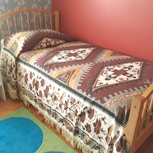 May include: A twin-sized bed with a white and brown patterned bedspread with fringe. The bedspread has a geometric design with brown, white, and gold accents.