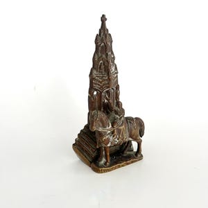 May include: A bronze figurine of a knight on horseback, with a detailed church spire on top. The knight is wearing armor and holding a sword. The church spire is ornate and has many windows and arches.