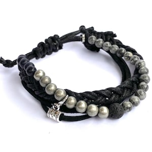 Puede incluir: Pulsera de cuero trenzado negro con cuentas plateadas y grises, una cuenta de lava negra y un dije plateado.