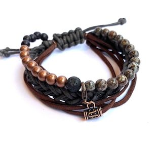 Puede incluir: Un brazalete de múltiples hebras con cordón de cuero marrón, cuentas negras y grises y un pequeño dije de metal.