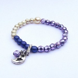 May include: A purple, blue and gold beaded bracelet with a crescent moon charm. The bracelet is made with iridescent glass beads.
