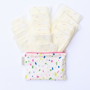 May include: A white zippered pouch with a colorful terrazzo pattern. The pouch is filled with white cloth pads, each with a small white circle with a number on it.