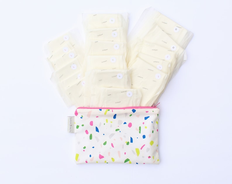 May include: A white zippered pouch with a colorful terrazzo pattern. The pouch is filled with white cloth pads, each with a small white circle with a number on it.