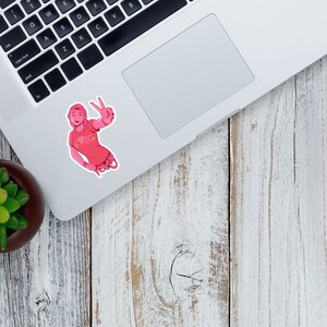 K&ouml;nnte beinhalten: Ein rosa Aufkleber mit einer Cartoon-Illustration einer Person, die ein Peace-Zeichen macht. Die Person tr&auml;gt ein rosa T-Shirt mit einem wei&szlig;en Design.