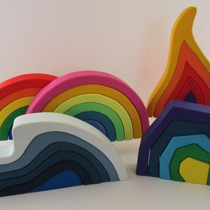 Puede incluir: Un conjunto de juguetes de apilar de madera arcoíris de colores. El conjunto incluye un arcoíris, una ola, una llama y un hexágono. Cada pieza está hecha de múltiples capas de madera, pintadas en diferentes colores.