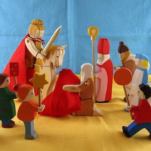 May include: A group of wooden figurines depicting a traditional Christmas scene. The figures include a knight on horseback, a bishop, a priest, and several children. The figures are painted in bright colors, including red, blue, yellow, and green.