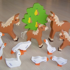 Può includere: Un set di animali giocattolo in legno, tra cui cavalli e oche, con un albero verde dipinto con pere. Gli animali sono dipinti in marrone e bianco.