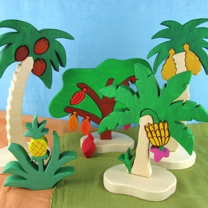 Puede incluir: Un conjunto de cinco árboles de juguete de madera, cada uno con una fruta o flor diferente. Los árboles están pintados en colores brillantes, incluyendo verde, marrón, amarillo, rojo y rosa. El conjunto incluye una palmera con cocos, un plátano con plátanos, un árbol de cacao con vainas de cacao, una planta de piña con una piña y un árbol floreciente con flores rosas.