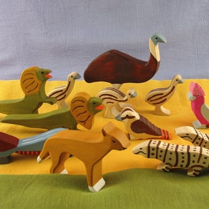 Peut inclure: Une collection de figurines d'animaux en bois, dont un émeu, un lézard, un kookaburra, un dingo et un lézard. Les figurines sont peintes dans des couleurs vives et présentent des détails réalistes.