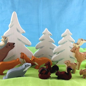 May include: A set of wooden animal figurines, including a deer, a badger, a fox, and squirrels, arranged around white wooden trees. The figurines are painted in realistic colours and have intricate details.