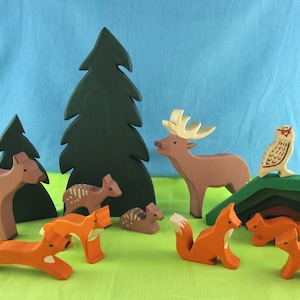 May include: A set of wooden animal figurines, including a deer, a fox, an owl, and a squirrel. The figurines are painted in brown, orange, and white. The set also includes two green trees and a brown log.