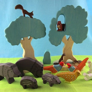 May include: A set of wooden animal figurines, including a squirrel, birds, and boars, arranged around two blue and green trees. The figurines are painted in various colors, including brown, red, and white.