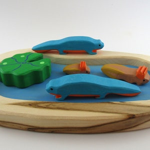 Könnte beinhalten: Ein Holzspielset mit einem Teich, einem grünen Seerosenblatt und vier blauen und orangefarbenen Salamandern. Der Teich ist von einem Holzrahmen umgeben.