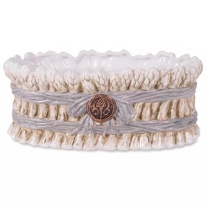 May include: An oval ceramic bowl featuring a sculpted exterior that resembles a bundle of asparagus stalks tied together with a grey ribbon. A circular brown medallion with a dark embossed emblem is centered on the front of the grey ribbon.