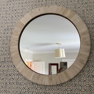 May include: A circular mirror with a light-coloured, segmented frame and a dark brown inner edge. The mirror reflects a room with a white ceiling, a light fixture, and a patterned wallpaper background.