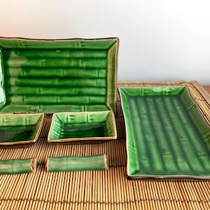 Peut inclure: Un ensemble de plats de service et de repose-baguettes en céramique verte. Les plats rectangulaires ont une texture de type bambou et une bordure marron. L'ensemble comprend des assiettes rectangulaires grandes et petites, et des plats carrés.