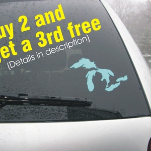 May include: A car's rear window with a yellow sticker that reads "Buy 2 and get a 3rd free (Details in description)". A blue outline of the Great Lakes is on the sticker.