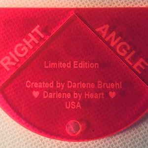 Puede incluir: Una plantilla de ángulo recto de plástico rojo con las palabras "RIGHT ANGLE" impresas en ella. Dice "Edición limitada" y "Creado por Darlene Bruehl Darlene by Heart USA".